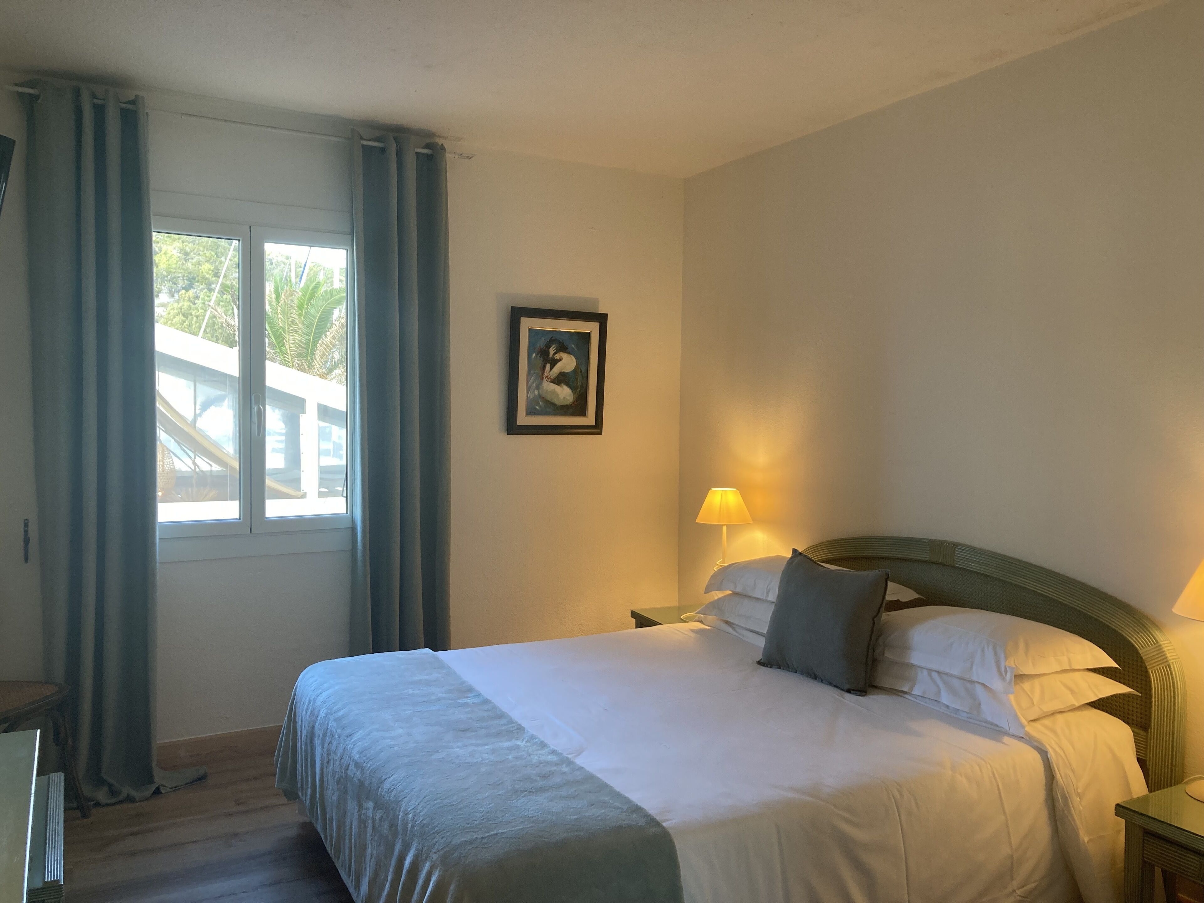 A hotel room with a large bed, a bedside lamp, a framed picture on the wall, and a window with curtains.