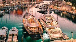 Een jachthaven met verschillende boten afgemeerd, een opvallend hoog schip in het midden en een historisch gebouw op de achtergrond.