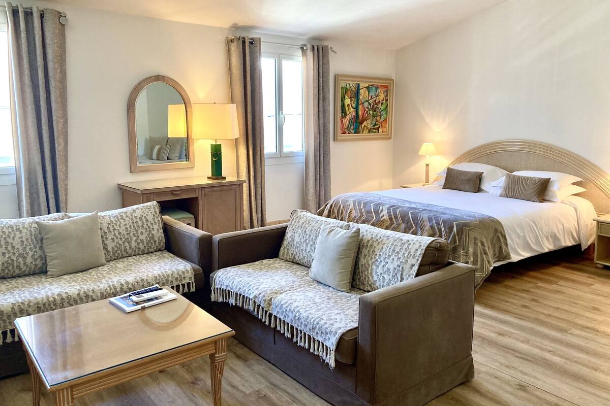 Habitación de hotel con sofá, cama, mesita de noche, lámpara, espejo y un cuadro.