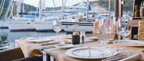 Mesa lista para comer con vistas a barcos y colinas al fondo.