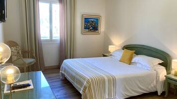 A hotel room with a bed, a chair, a table with a lamp, a painting on the wall, and a window with curtains.