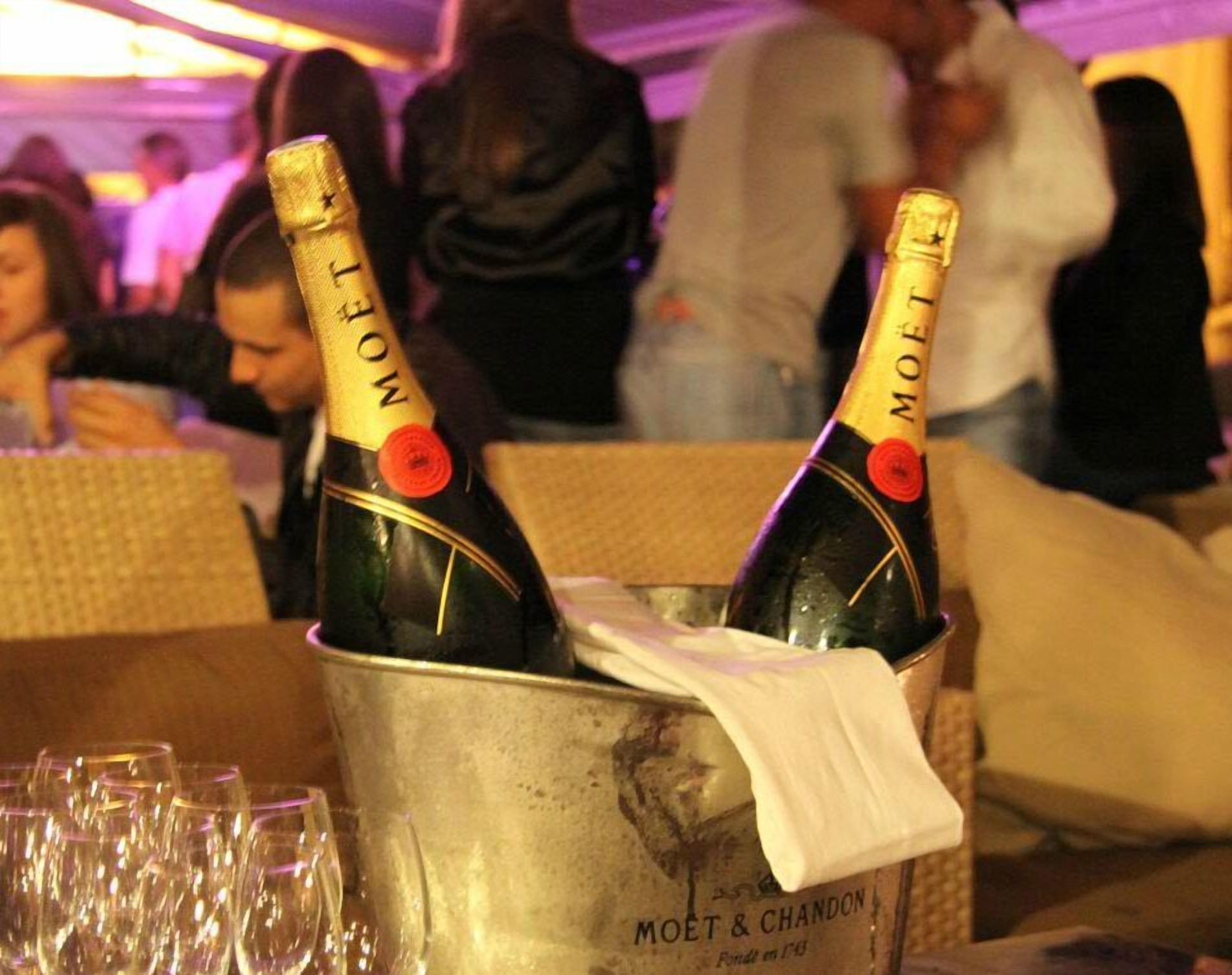 Two champagne bottles in a metal bucket with glasses around them.