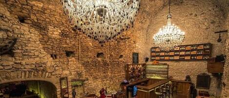 A spacious lounge with stone walls, a large chandelier, leather seating, and a bar area.