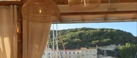 An outdoor dining area with wicker chairs and tables, overlooking a marina with boats and buildings.