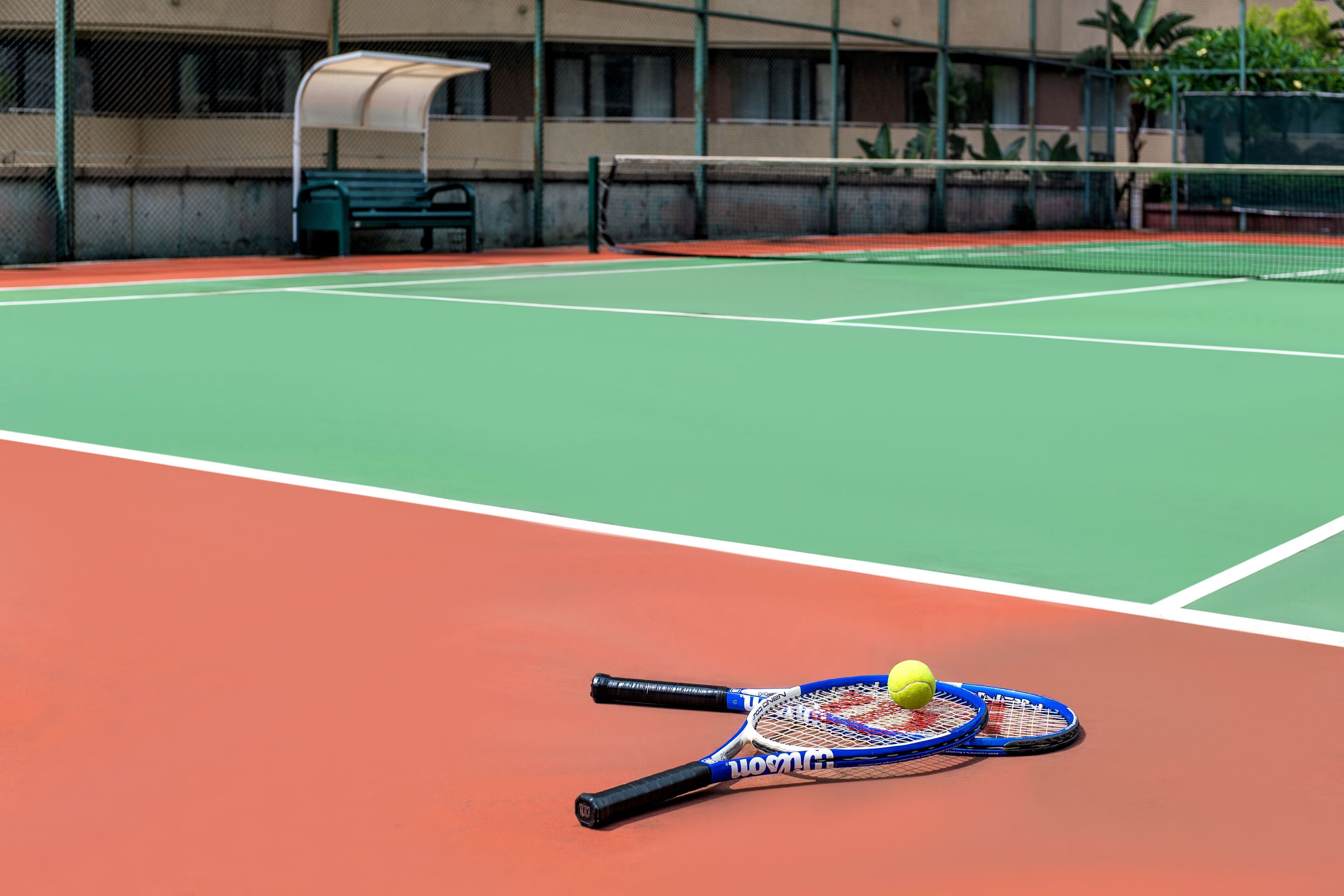 A tennis court with a net, two tennis rackets, and a tennis ball.