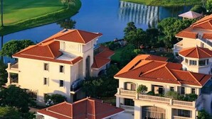 Un campo de golf con un elemento acuático, rodeado de edificios residenciales con techos de tejas rojas.