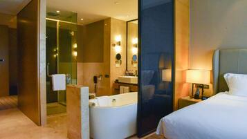 Habitación de hotel con una bañera grande, zona de ducha separada, cama y mesita de noche con lámpara.