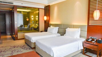 Habitación de hotel con dos camas, una mesita de noche con teléfono y lámpara, y un espejo grande que refleja parte de la habitación.