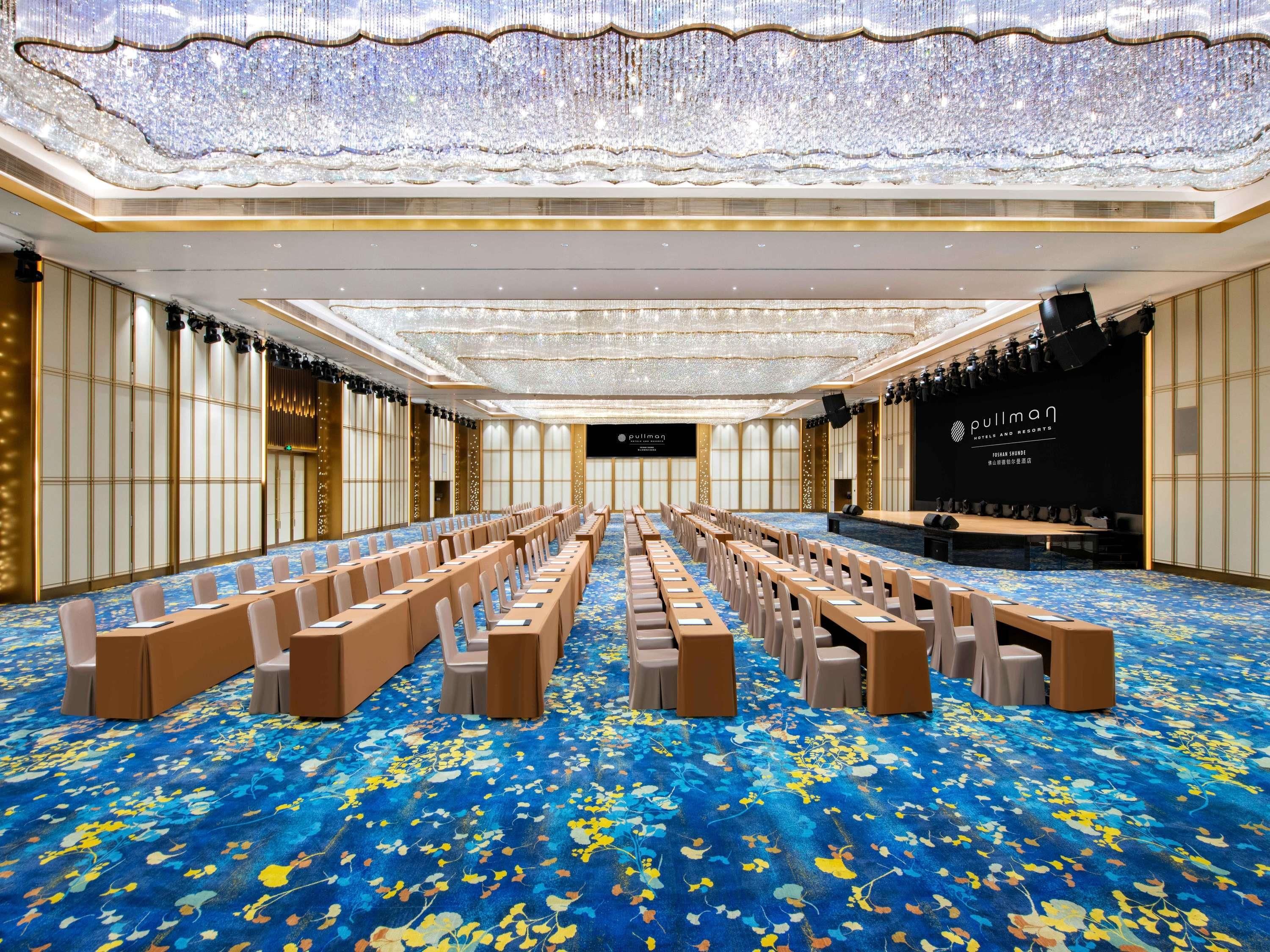 Een grote congreszaal met rijen stoelen, een podium en een kroonluchter.