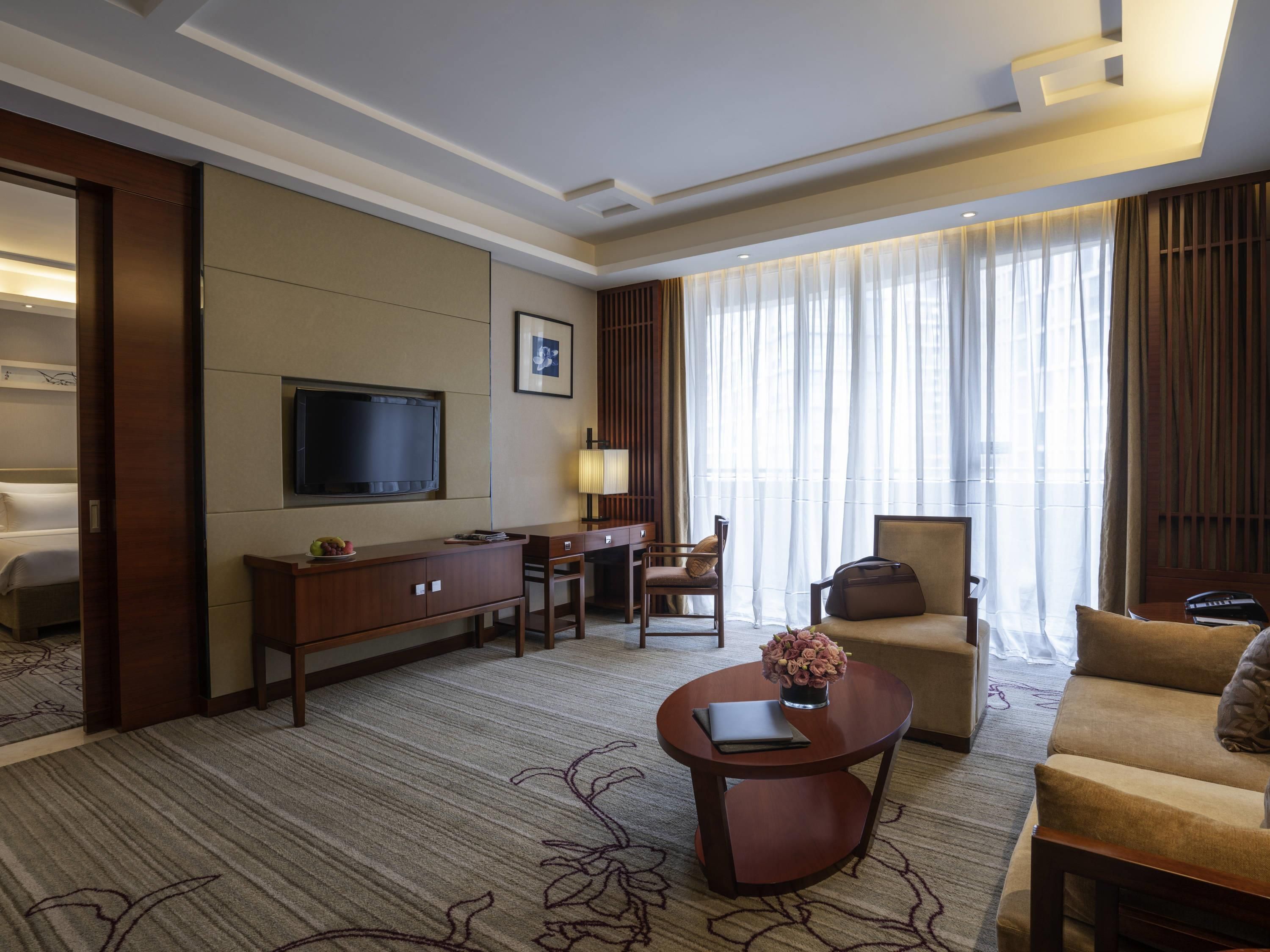 Habitación de hotel con cama, televisor, escritorio, silla, sofá y mesa de centro.