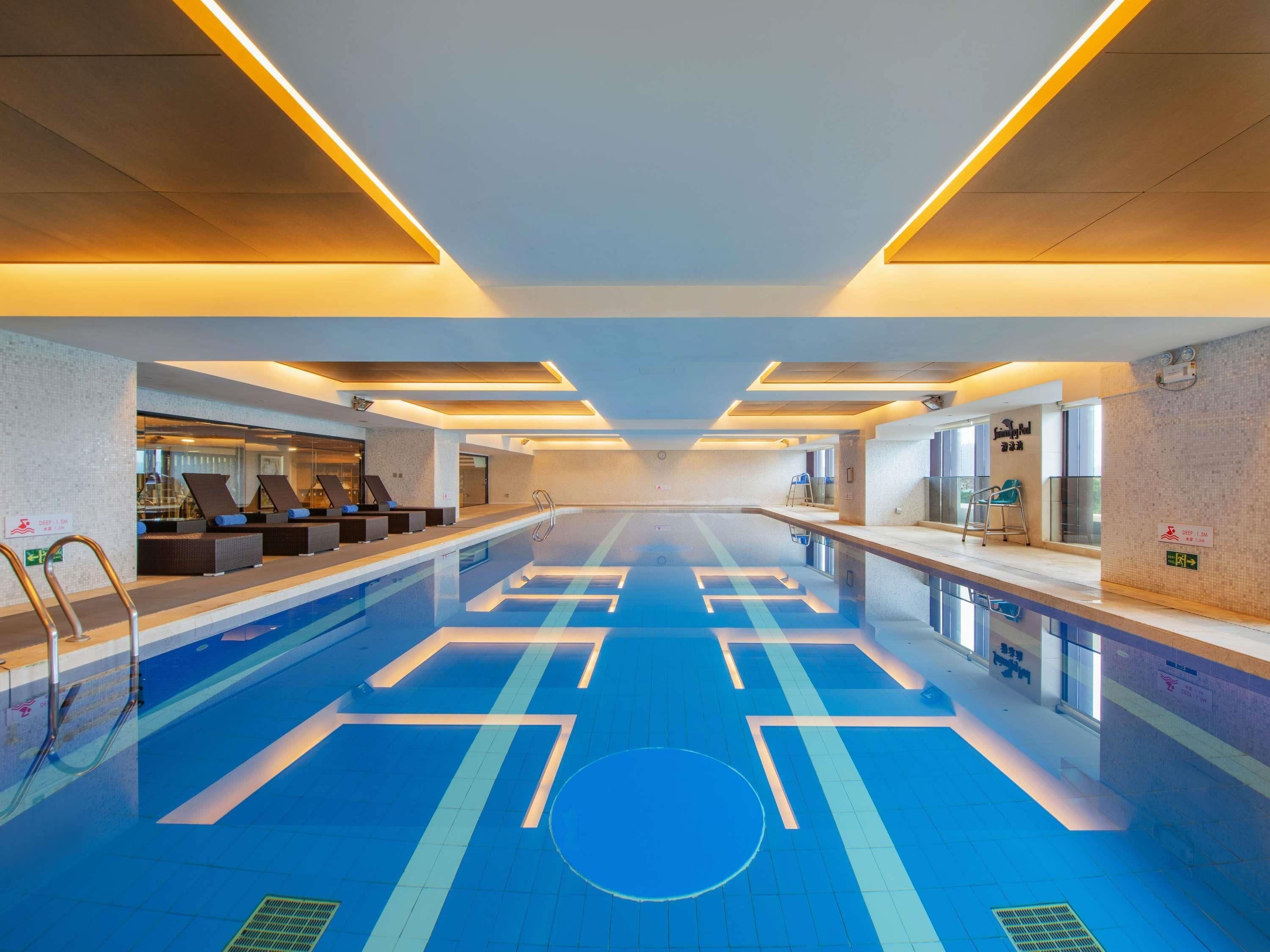 An indoor swimming pool with clear lane markings, a lounge area with seating, and a reception desk.
