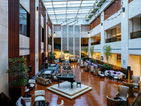 A spacious atrium with a grand piano, multiple seating areas, and a high ceiling with natural light.