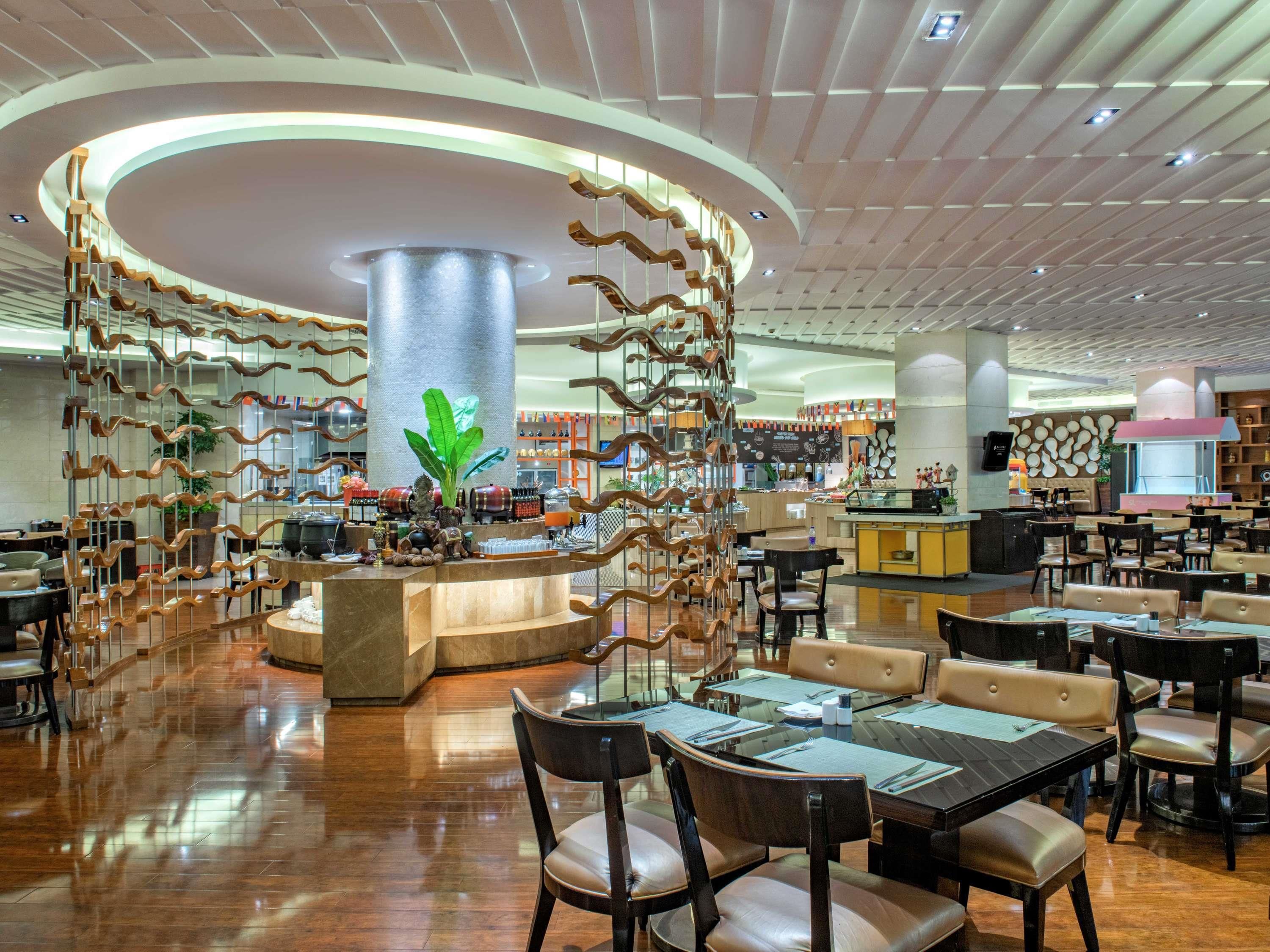 Un restaurante espacioso con una isla central, varias zonas de estar y un diseño moderno en el techo.