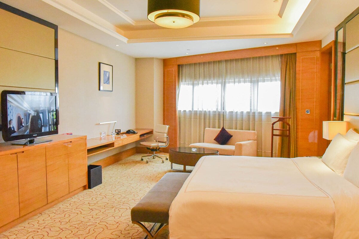 Una habitación de hotel con una cama grande, un escritorio con una silla, televisión y una ventana con cortinas.