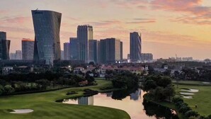 Un paisaje urbano con rascacielos modernos y un campo de golf con un lago tranquilo que refleja los edificios.