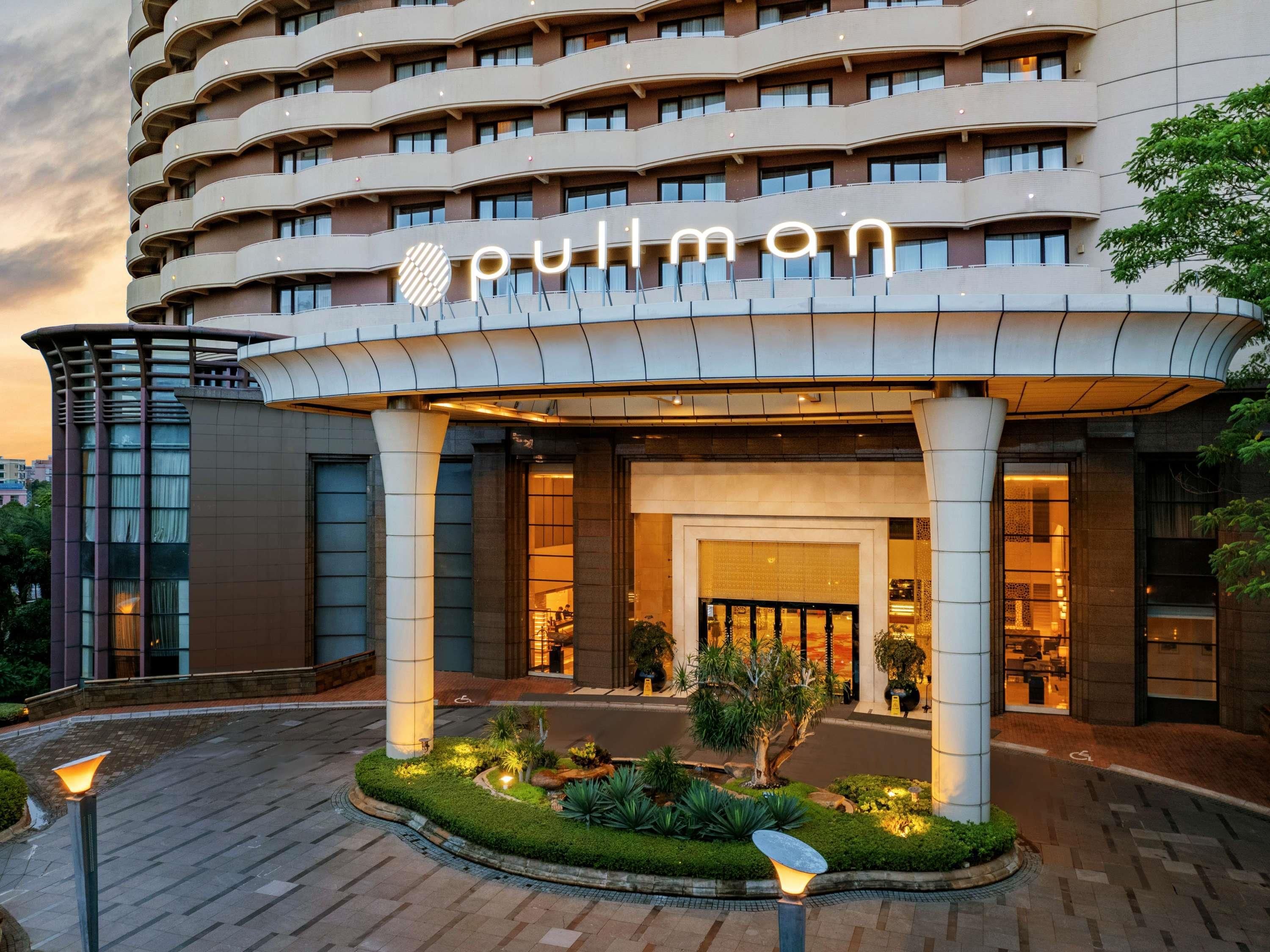 A hotel entrance with a curved facade, a prominent 'pullman' sign, and a landscaped garden area.