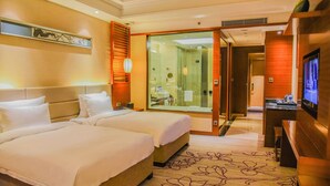 Habitación de hotel con dos camas, un televisor y un baño visible a través de una puerta de vidrio.