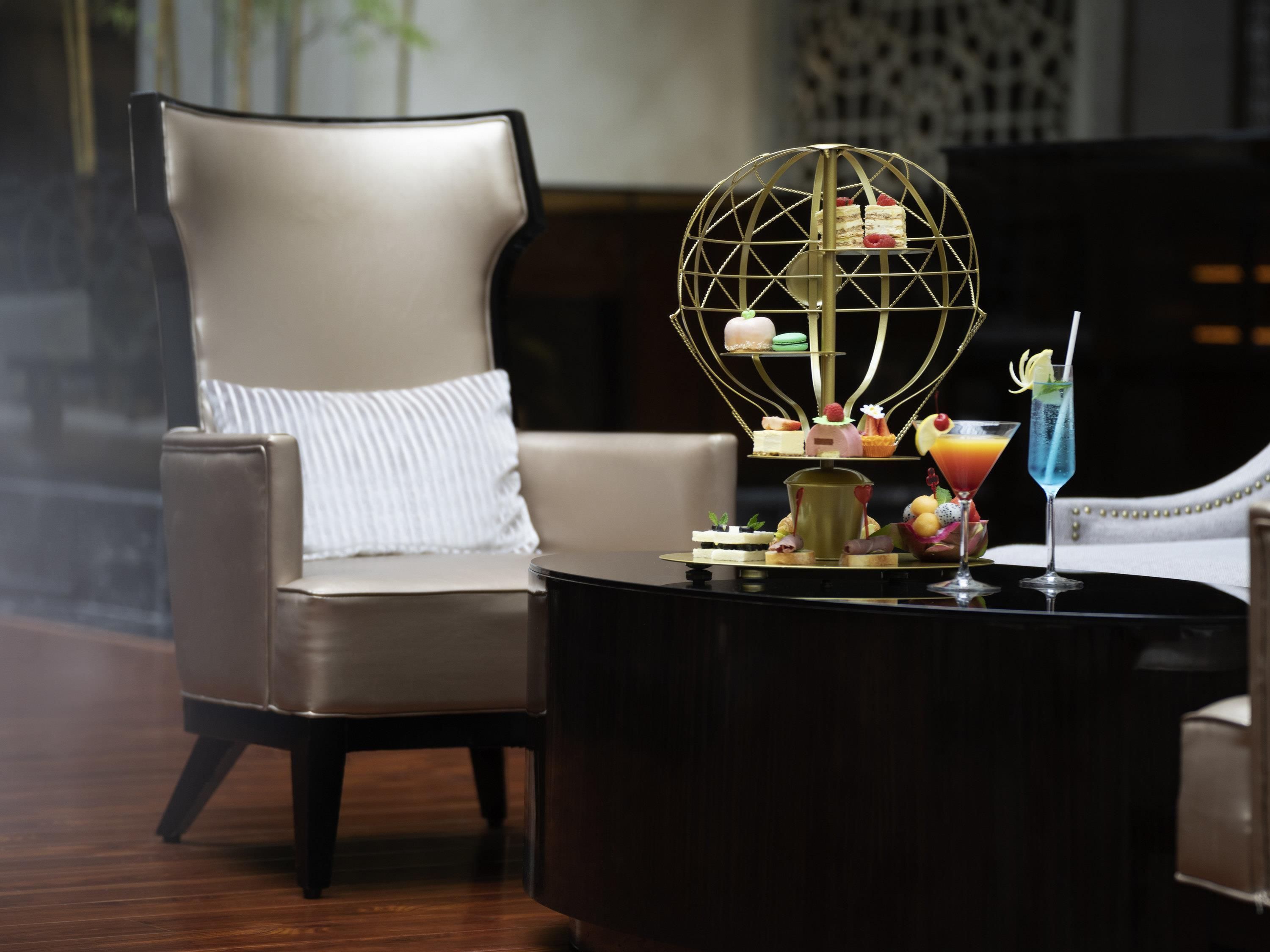 A modern lounge area with a leather armchair, a round coffee table with desserts and drinks, and a decorative metal sphere.