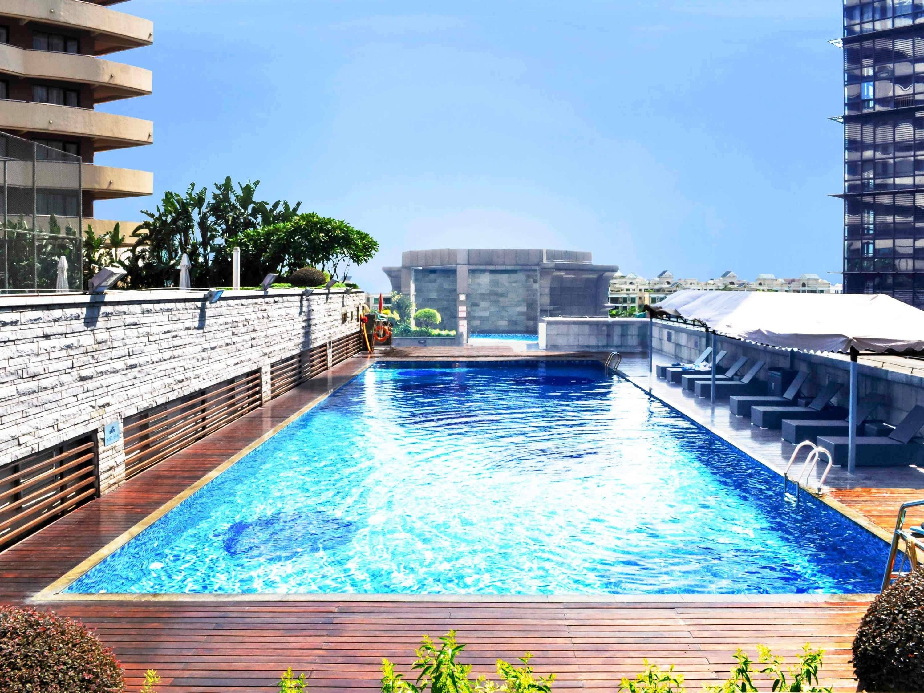 Una piscina en la azotea con cubierta de madera, rodeada de edificios y vegetación.