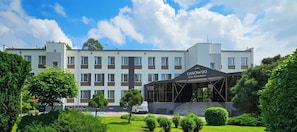 Hotel com fachada moderna, entrada coberta e jardim bem cuidado.