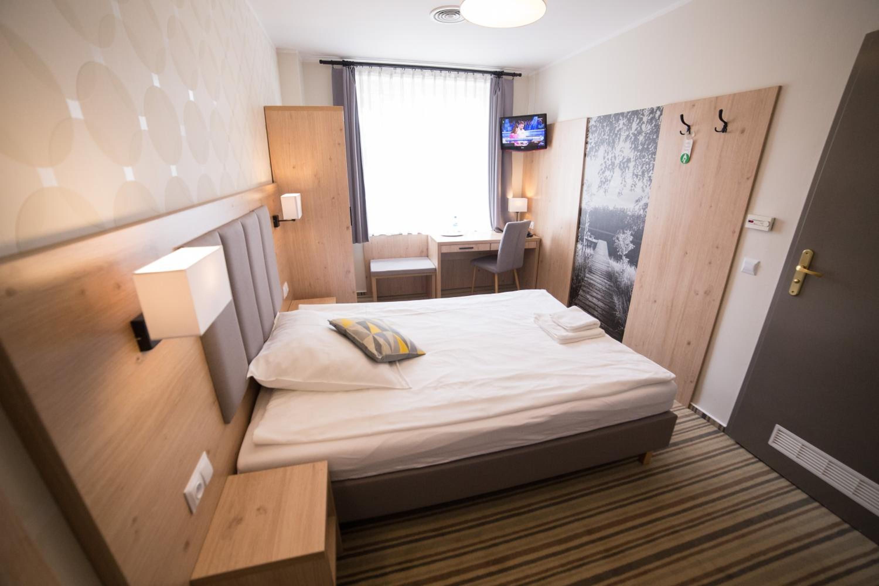 A hotel room with a bed, a desk, a chair, a television, and a door.
