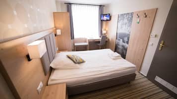 A hotel room with a bed, a desk, a chair, a television, and a door.