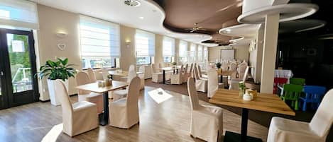 A restaurant with a modern interior, featuring wooden tables and chairs, large windows, and a ceiling with circular light fixtures.