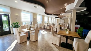 Restaurante com interior moderno, destacando mesas e cadeiras de madeira, janelas amplas e teto com luminárias circulares.