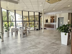 Uma área de recepção moderna, com balcão, espaço para sentar e amplas janelas.