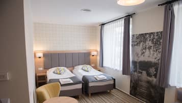 A hotel room with two beds, a small table, a chair, and a large window with curtains.