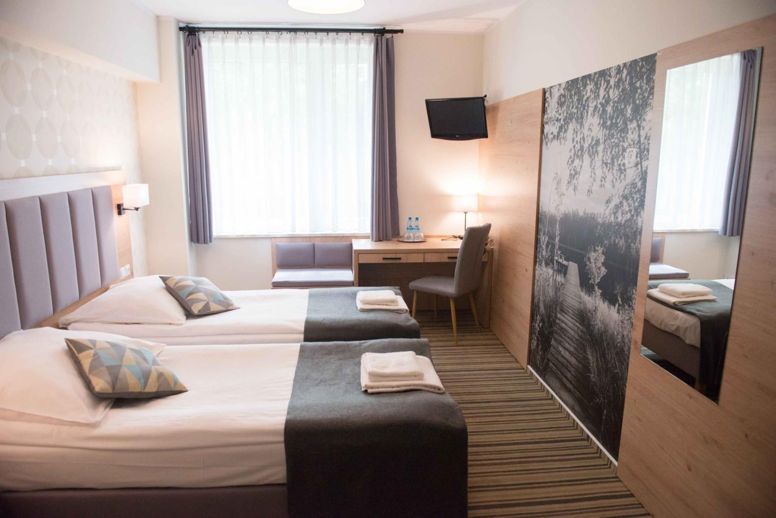 Ein Hotelzimmer mit zwei Betten, einem Schreibtisch, einem Stuhl, einem Flachbildfernseher und einem großen Poster an der Wand.