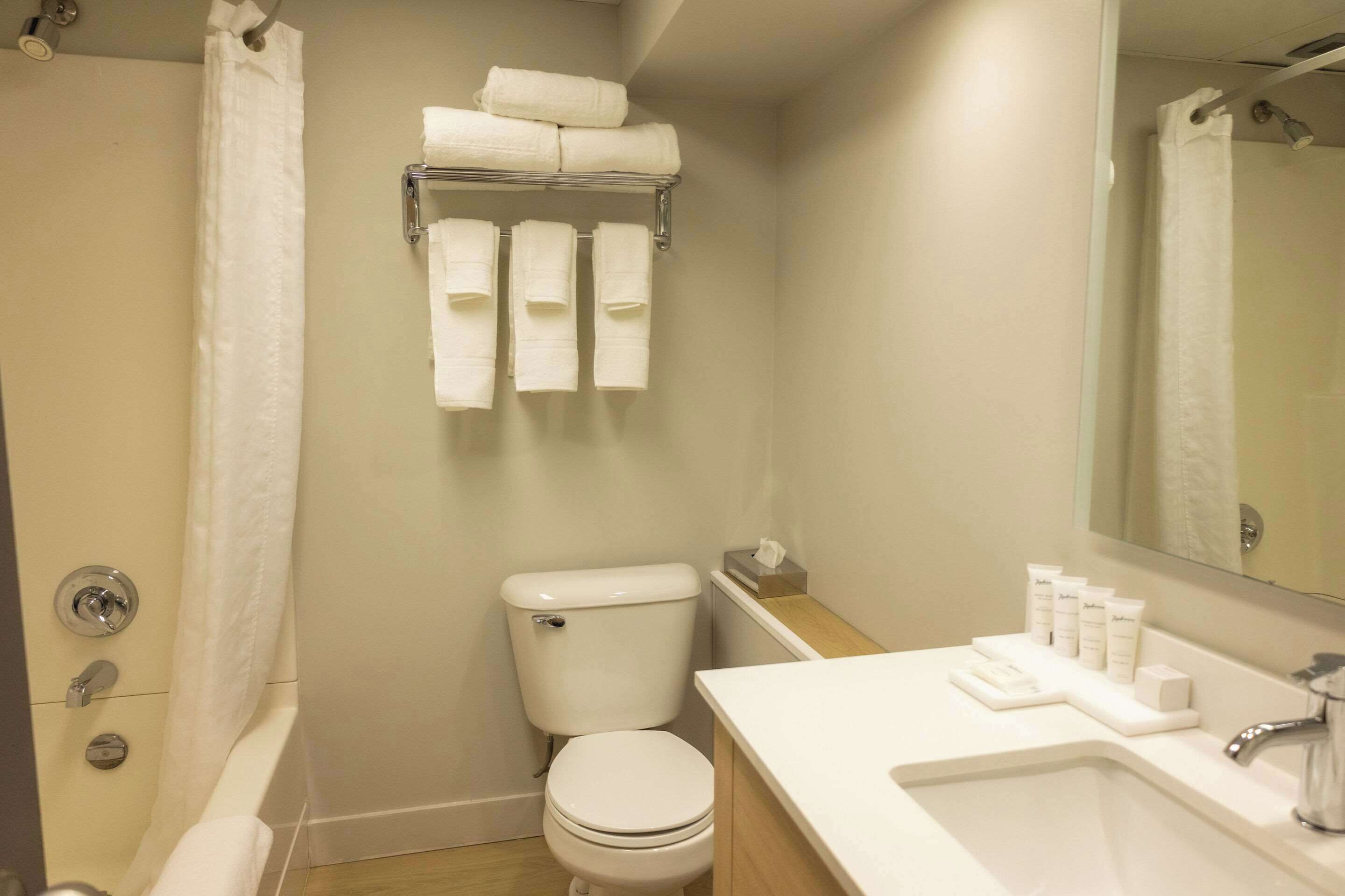 Ein Badezimmer mit Toilette, Waschbecken und Dusche. Handtücher und Pflegeprodukte liegen am Waschbecken.