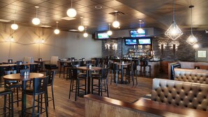 Ein Restaurant mit verschiedenen Sitzbereichen, darunter gemütliche Nischen, Tische und eine Bar mit rustikaler Steinwand, ergänzt durch hängende Pendelleuchten.