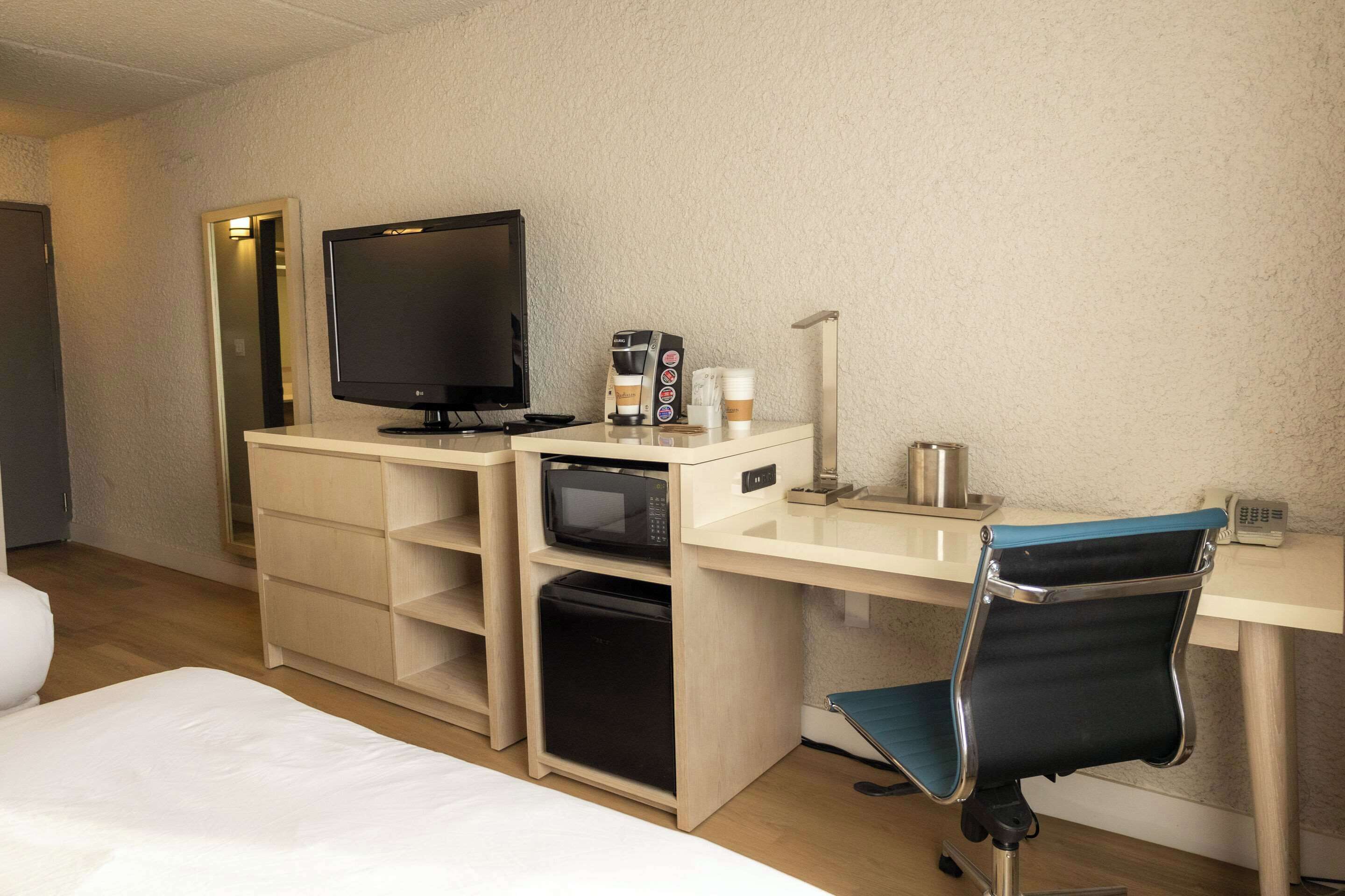 A hotel room with a bed, a desk with a computer, a television, a microwave, a coffee maker, and a chair.
