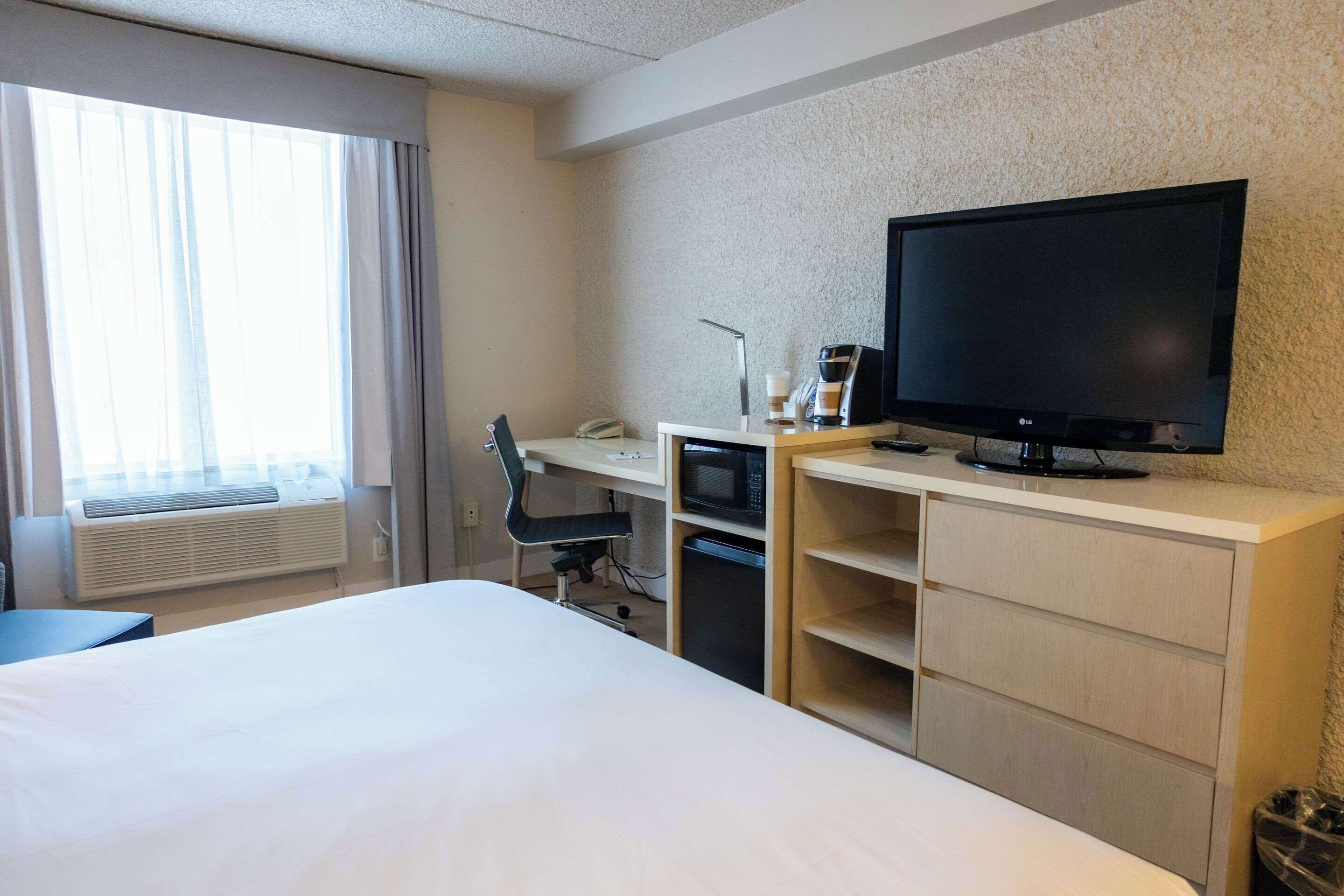 A hotel room with a bed, a desk with a computer, a TV, and a window with curtains.