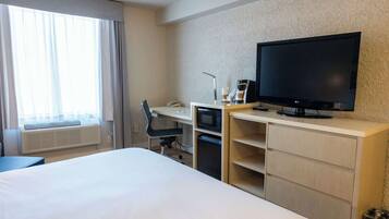 A hotel room with a bed, a desk with a computer, a TV, and a window with curtains.