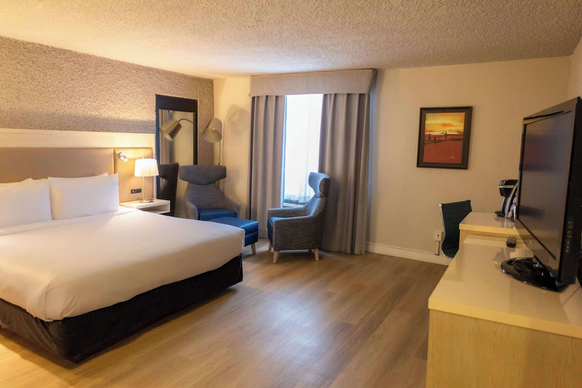 A hotel room with a large bed, a desk with a computer, a chair, a lamp, and a painting on the wall.