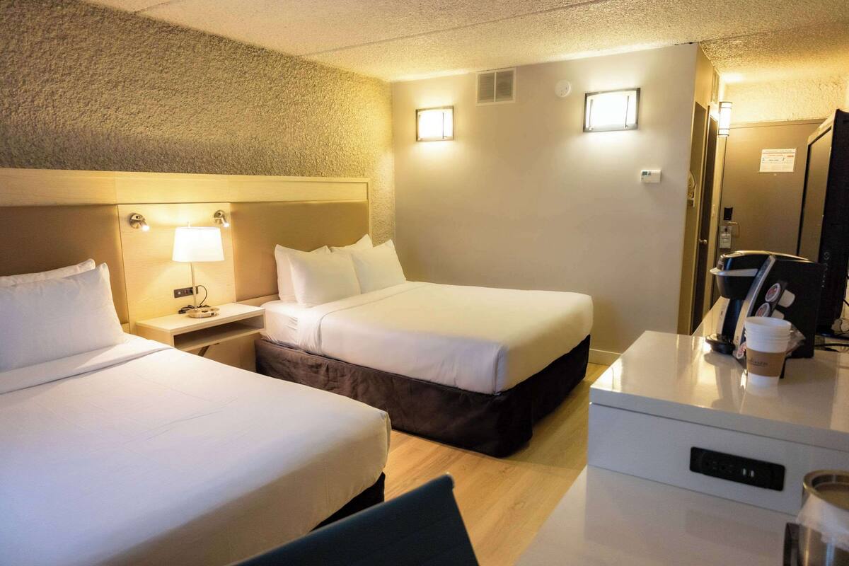 A hotel room with two beds, a desk, a chair, a coffee machine, and a TV.