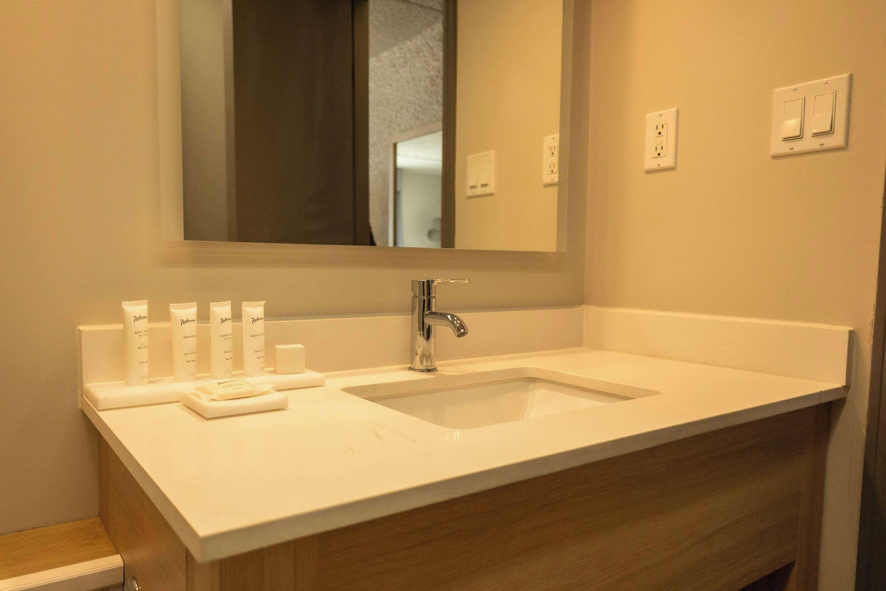 Un baño con lavamanos blanco, espejo y tocador de madera.