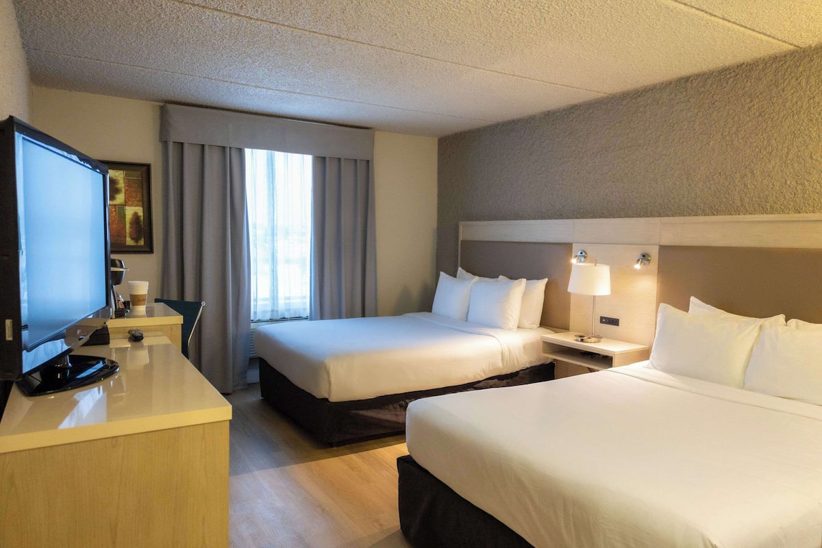 A hotel room with two beds, a desk with a television, and a window with curtains.