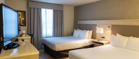 A hotel room with two beds, a desk with a television, and a window with curtains.