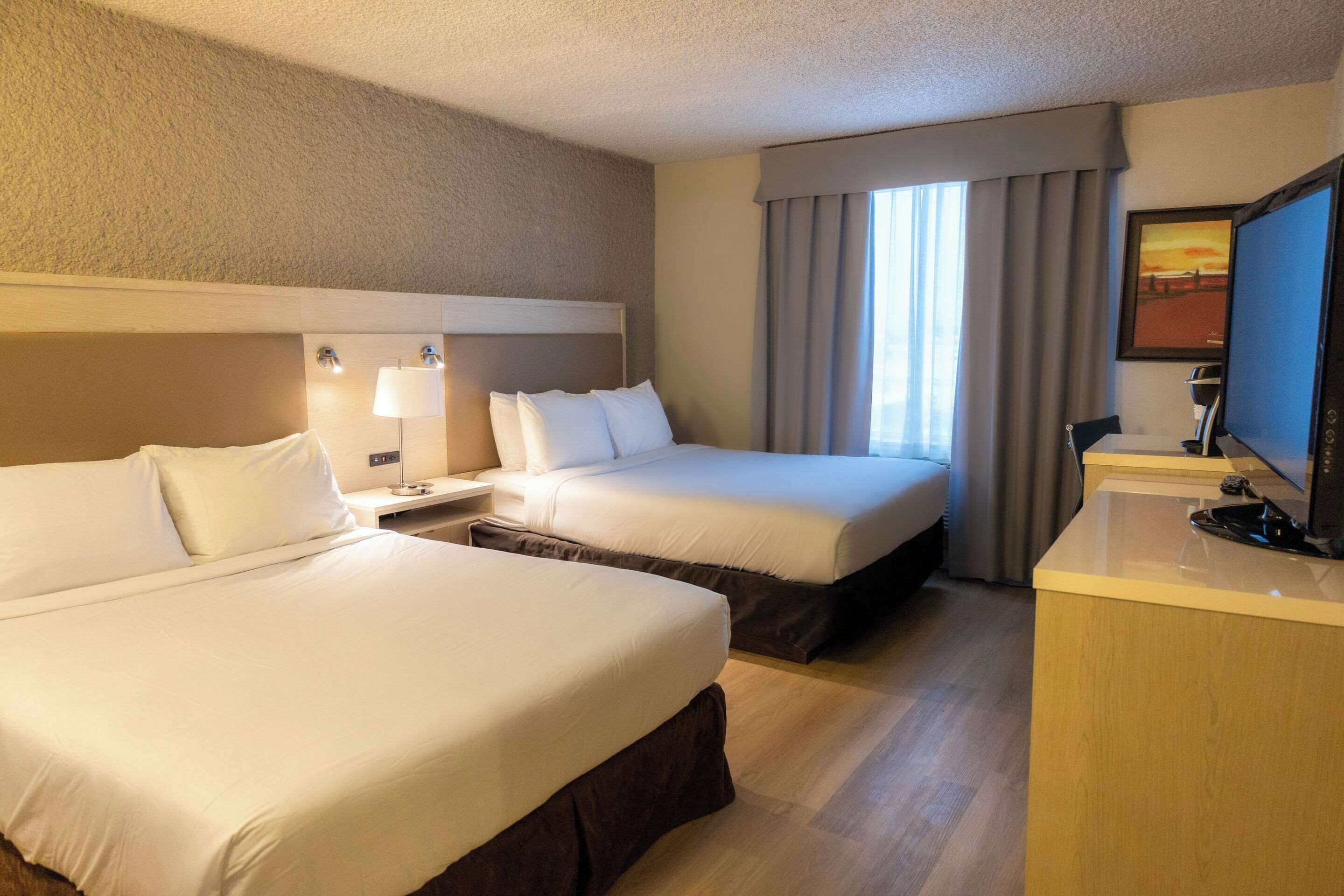 A hotel room with two beds, a desk, a television, and a window with curtains.