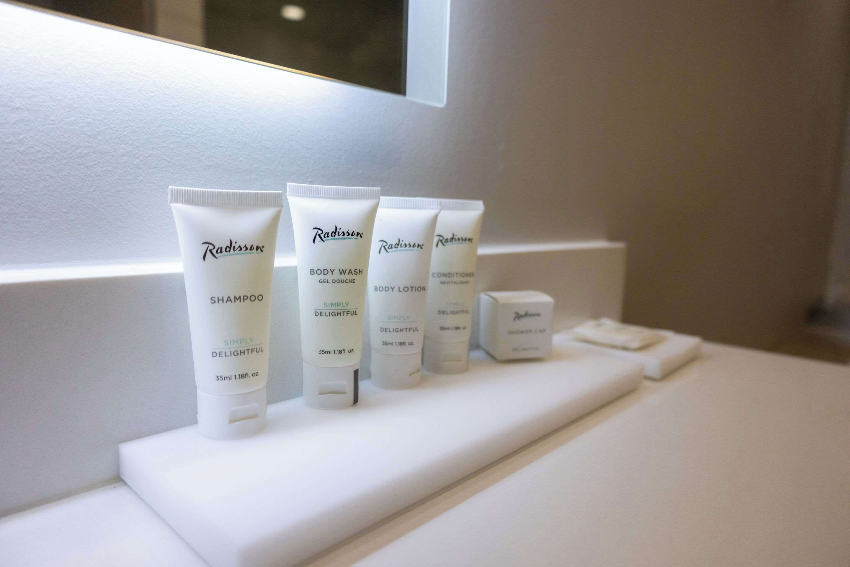 A bathroom shelf with four Radisson body care products: shampoo, body wash, body lotion, and conditioner.