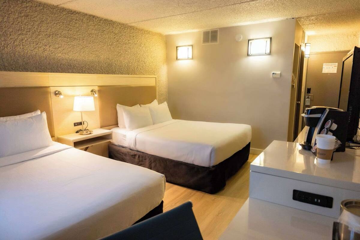 A hotel room with two beds, a desk with a lamp, a coffee machine, and a TV.