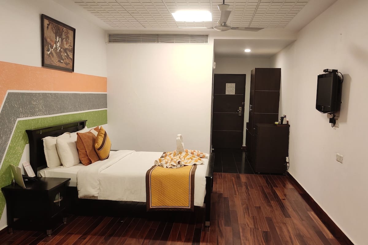 Een slaapkamer met een bed, nachtkastje en een aan de muur bevestigde televisie.