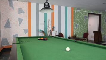 A pool table with balls and a cue stick, a lamp, and chairs in a room with striped walls.