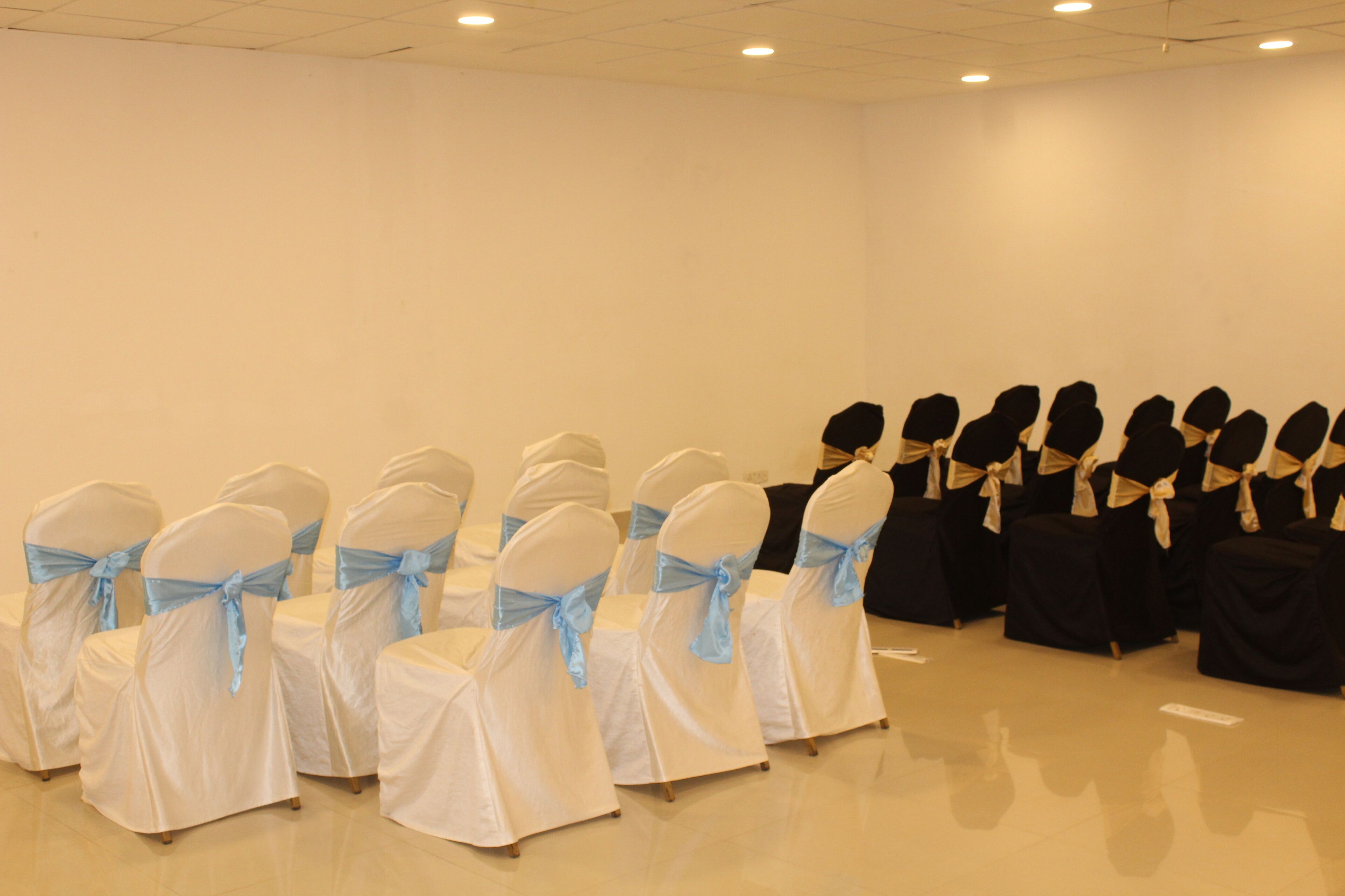 Une salle de conférence avec des rangées de chaises, certaines recouvertes de tissu blanc et d'autres de tissu noir, et agrémentées de rubans bleus.