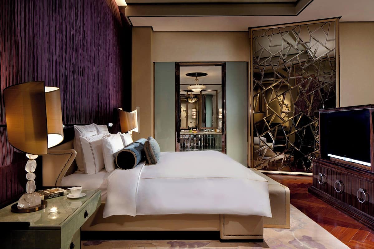 A modern hotel room with a large bed, a television, and a decorative wall.