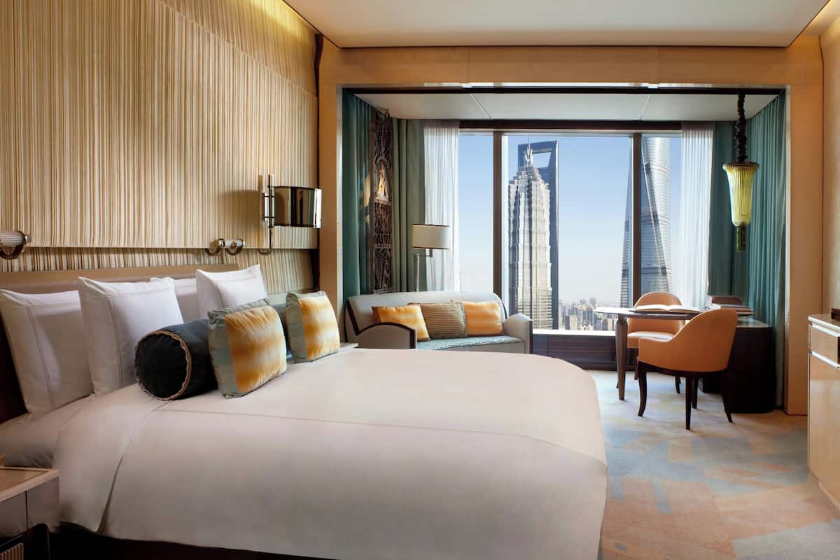 A hotel room with a large bed, a desk, and a view of a cityscape.