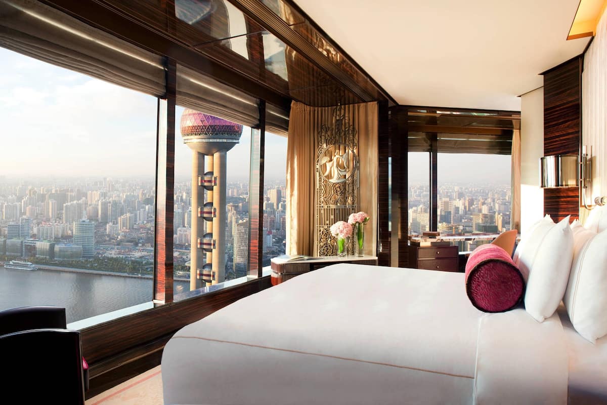 A high-rise hotel room with a large bed, a desk, and a view of a cityscape and a tower.